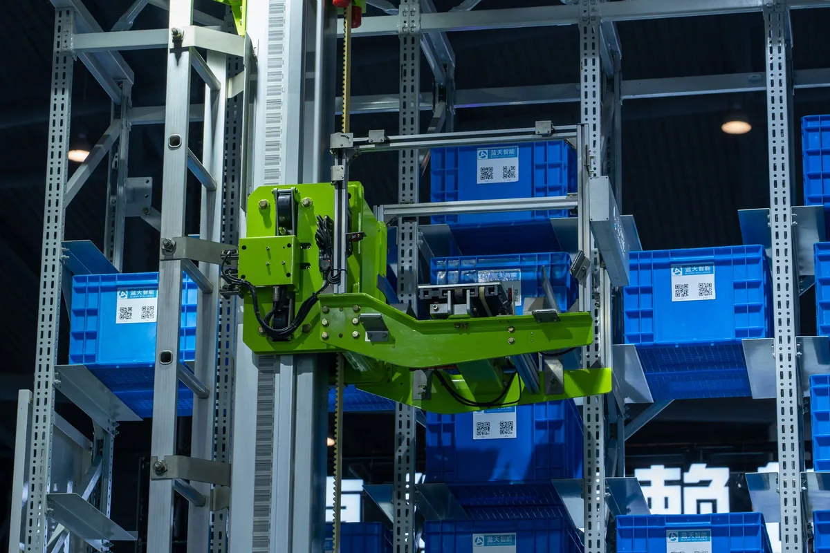Automated stacker crane and robotic handling system moving blue crates in a high-bay warehouse