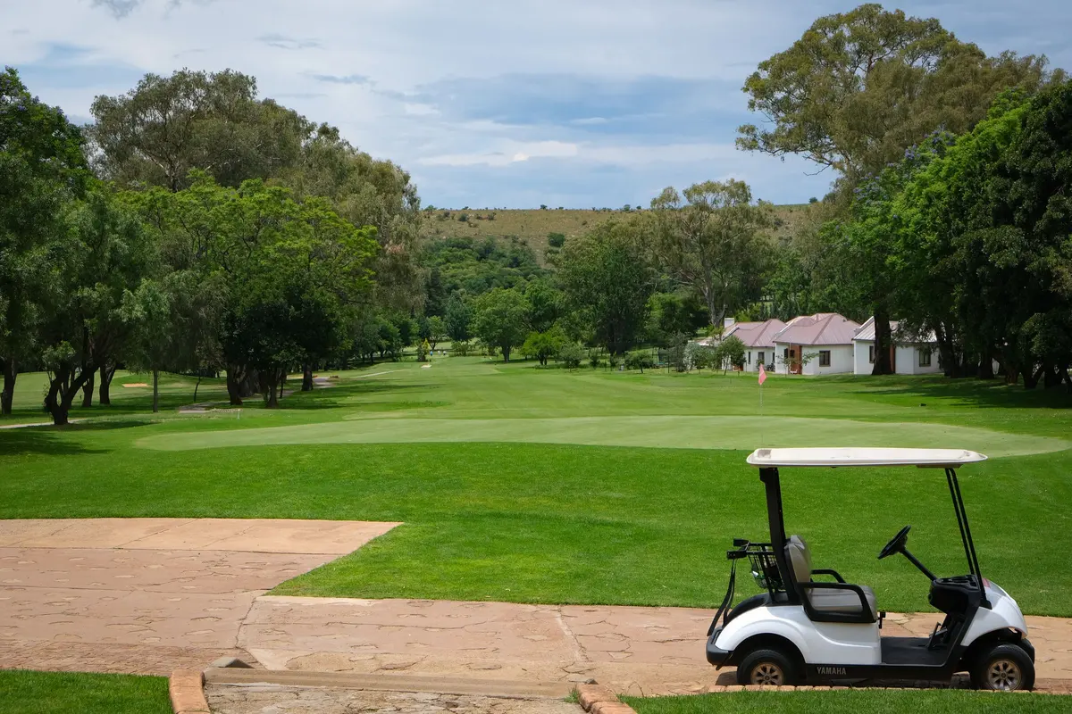 Golf cart on a hilly course fairway with a clubhouse in the background